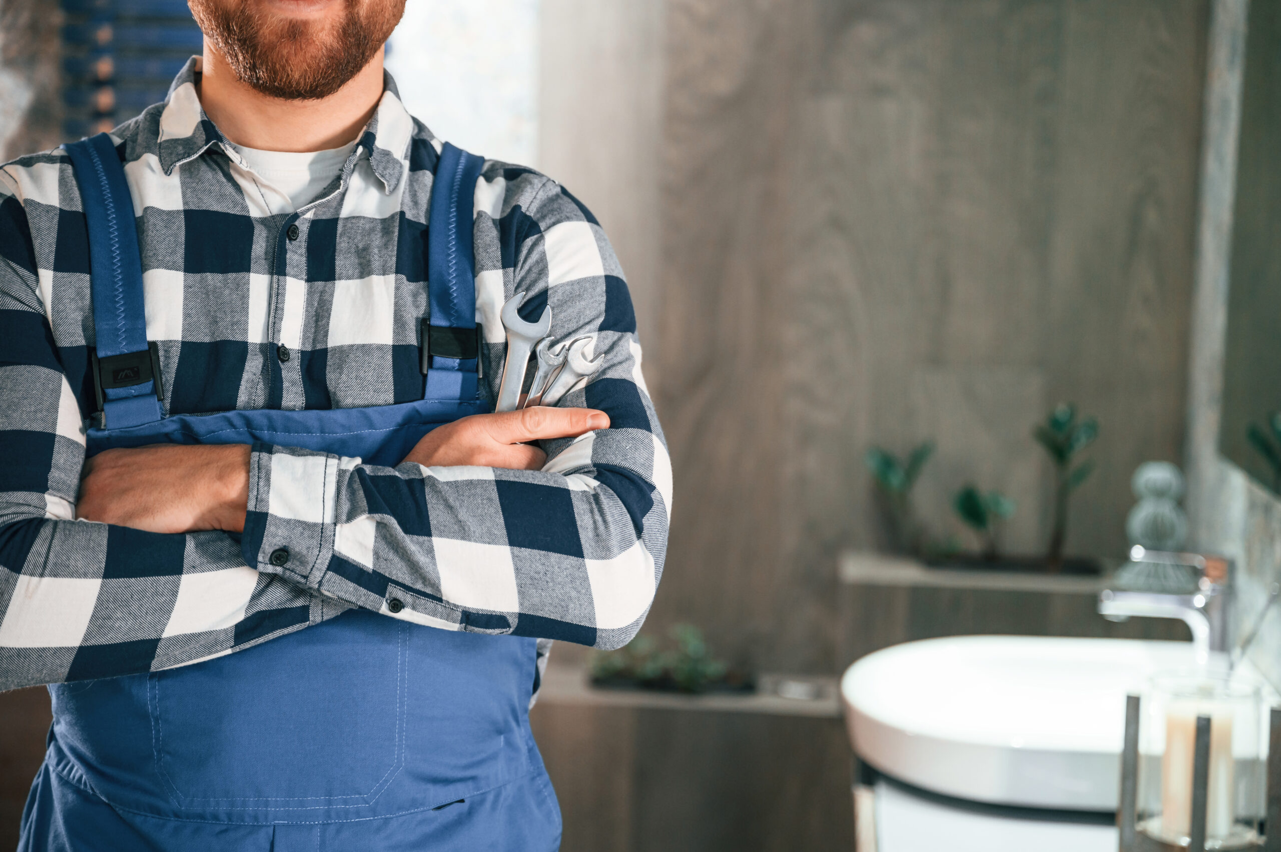 Standing with arms crossed. Plumber in blue uniform is at work in the bathroom.